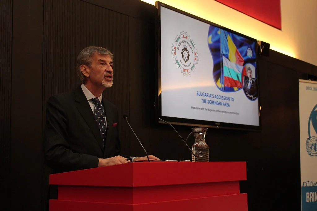 Konstantin Dimitrov speaking at a lectern at one of the society's events, beside a slide on Bulgaria's accession to the Schengen area.