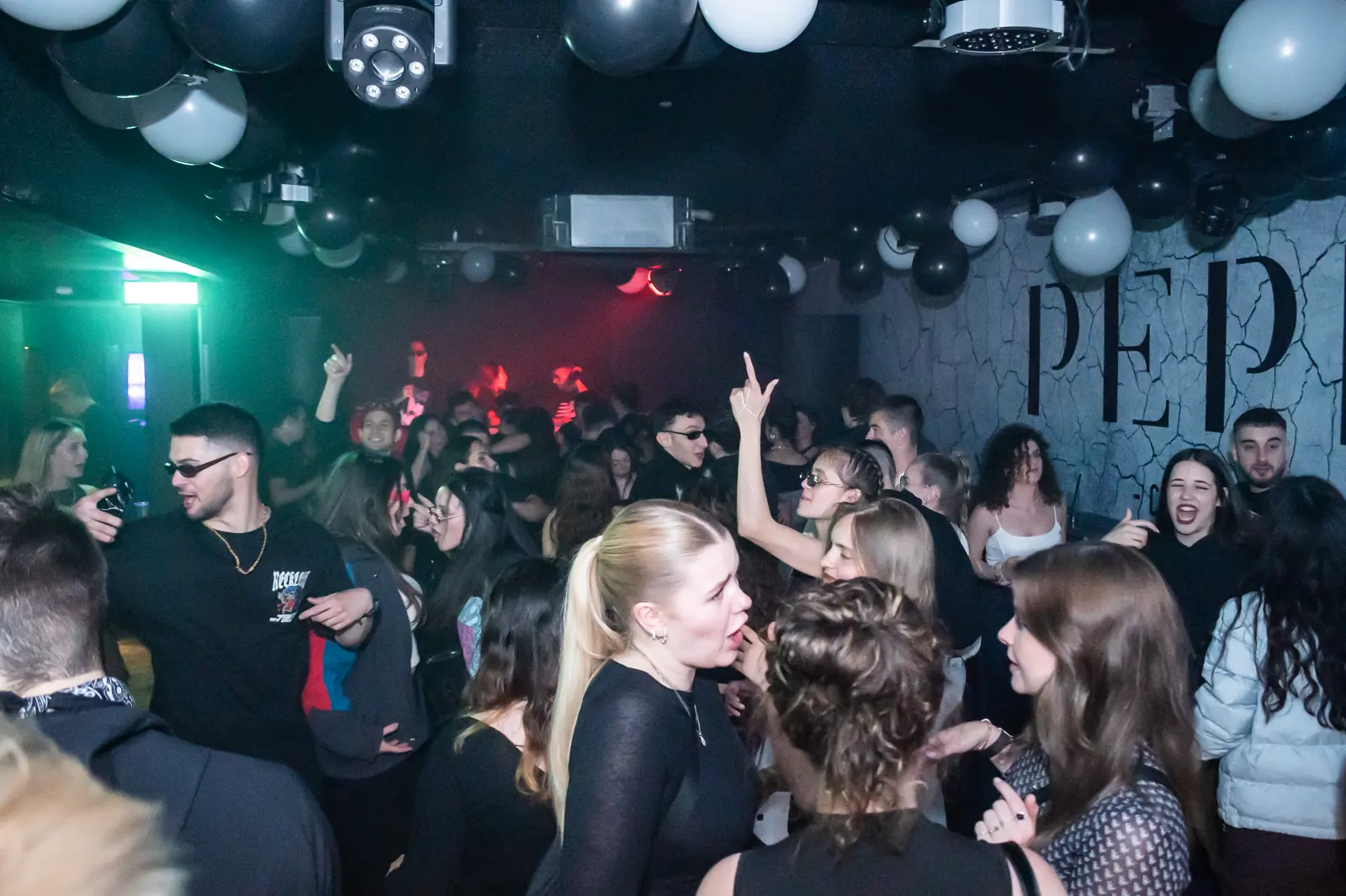 A packed floor at PEPR under green and red light, balloons across the ceiling.