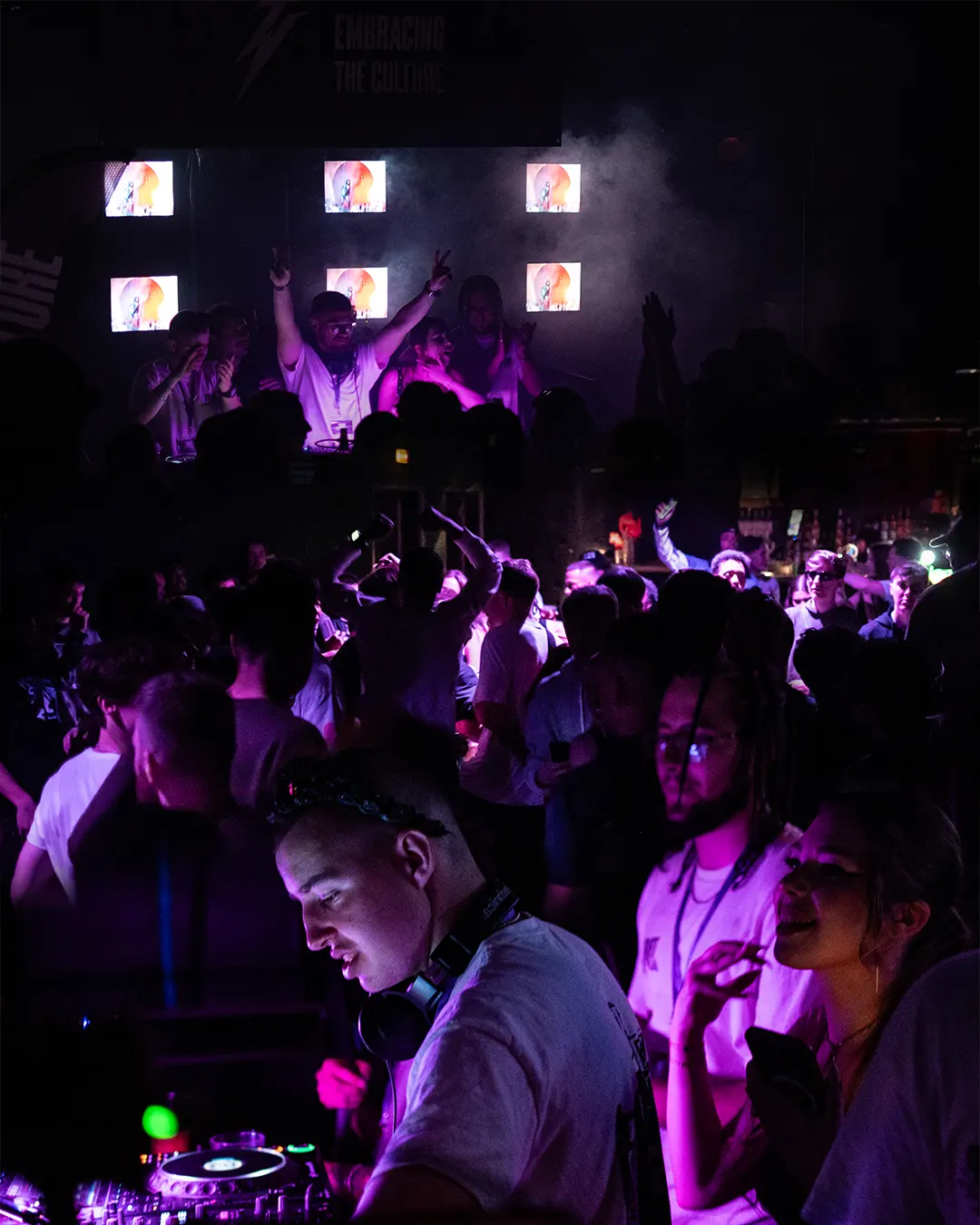 A DJ behind the decks at OOST, the screen grid lit behind him.