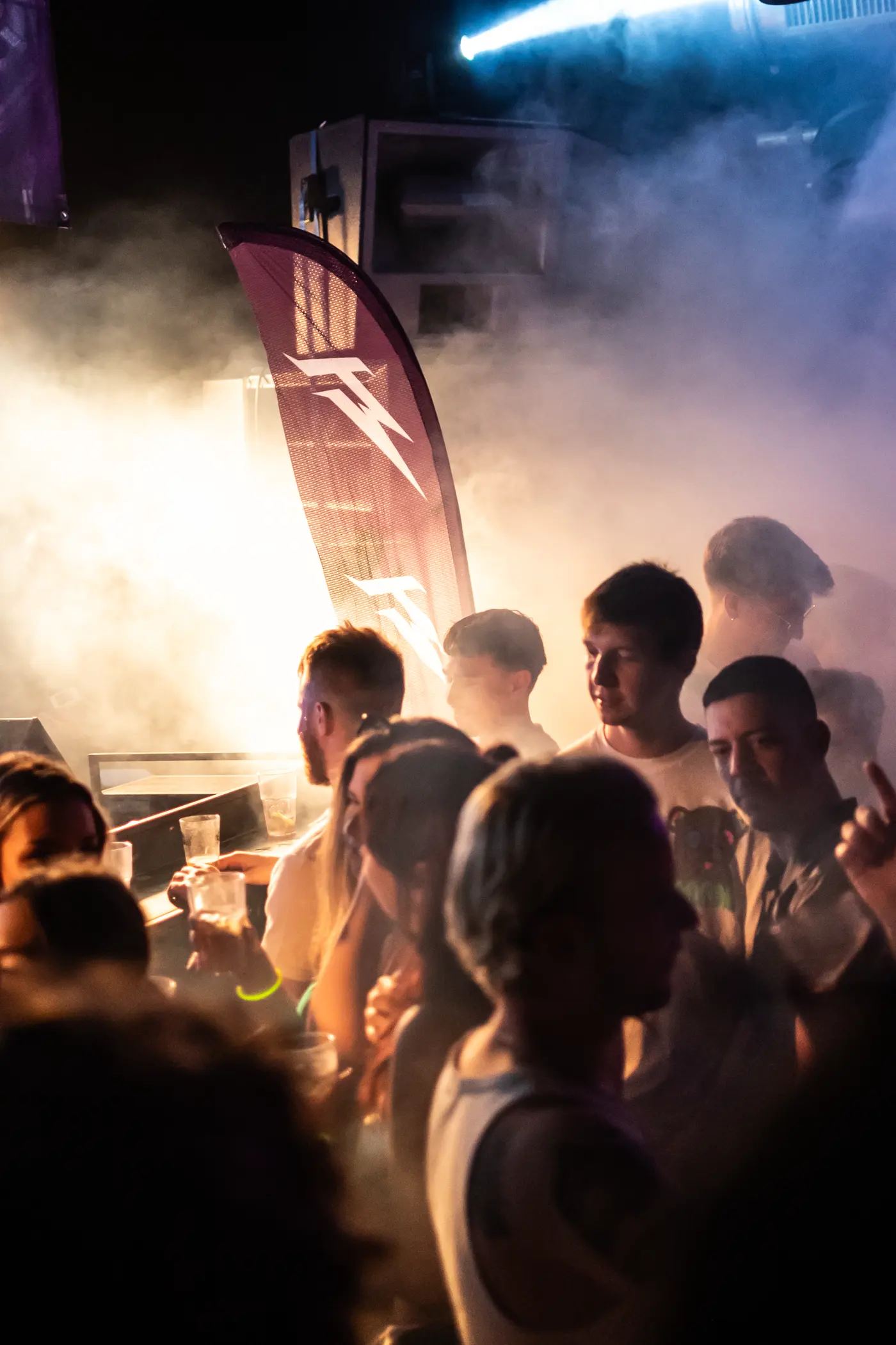 A flag standing in the smoke beside the booth, crowd in front of it.